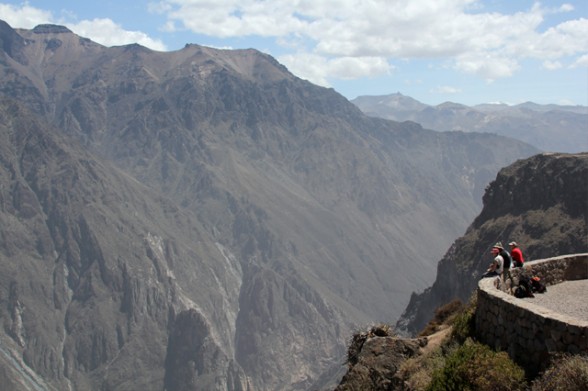 three tourists sitting at the edge of peru's colca canyon