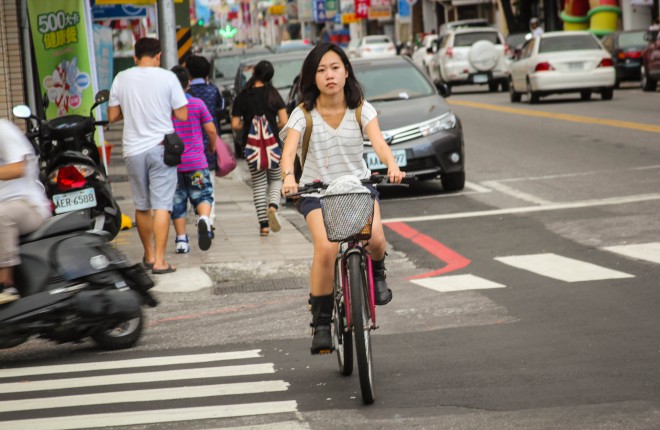 young taiwanese girl riding a bicycle across the street