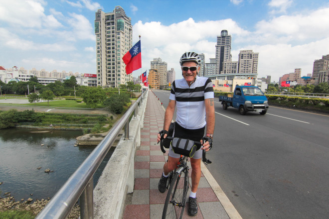 Kevin Burrett cycles with taiwan flags in background of Taipei