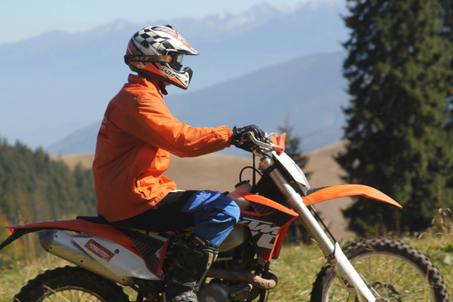 man in orange jacket riding a ktm motorcycle off road in romanian mountains