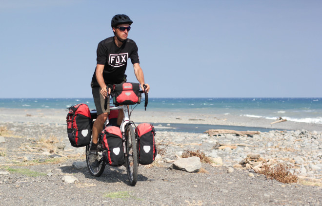Man in black clothing riding a bicycle along the beach in Asia
