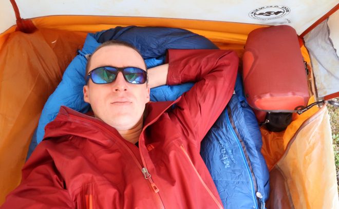 Darren Alff wears blue sunglasses and sleeps on sleeping bag inside tent during 2017 bike tour across Sweden, Norway and Finland