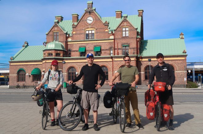 Four male and female bicycle travelers standing with their bikes in front of the Umea, Sweden train station